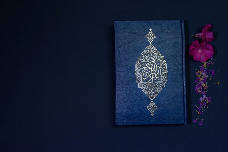 A closed Qur’an beside flowers on a dark blue background